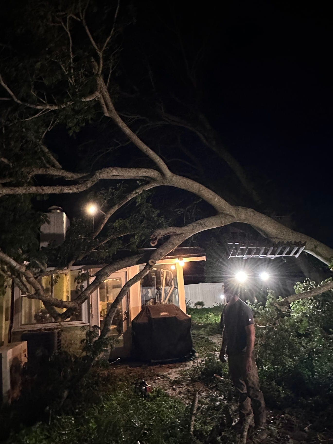 T.E.A.M. crew member working under headlamps to clear a tree fallen onto a Tampa Bay home at night