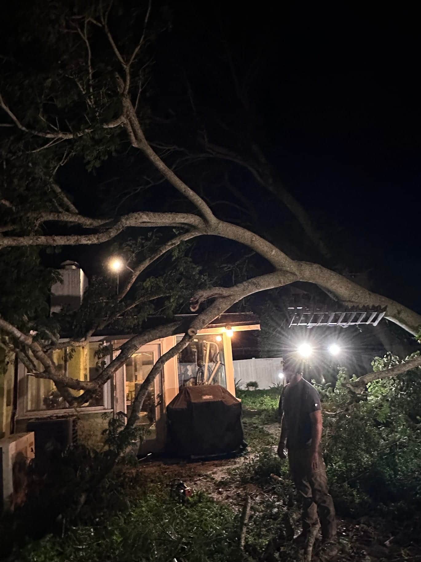 T.E.A.M. crew member working under headlamps to clear a tree fallen onto a Tampa Bay home at night