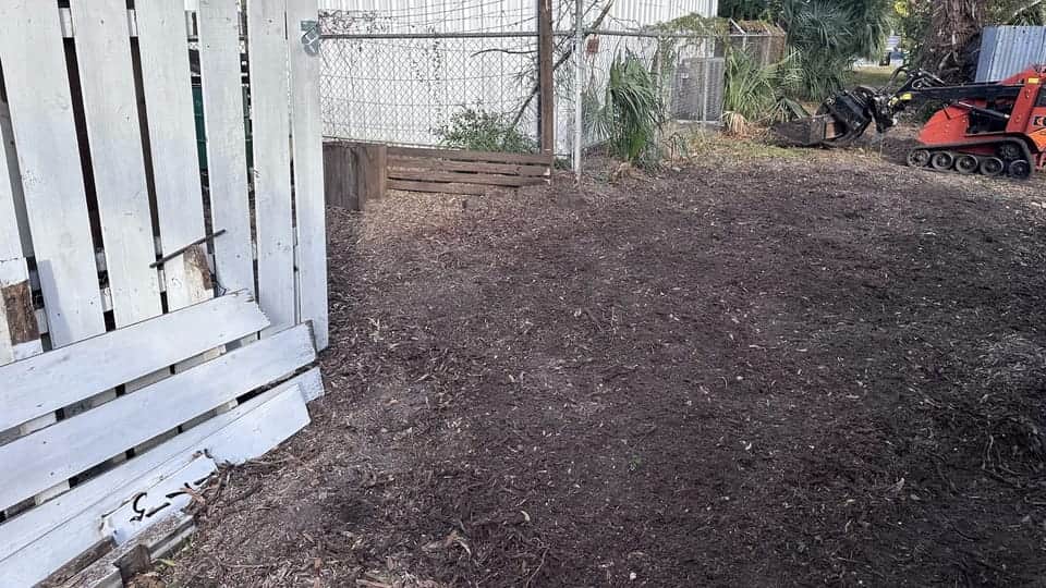 Tracked loader beside a cleared section of property after brush removal