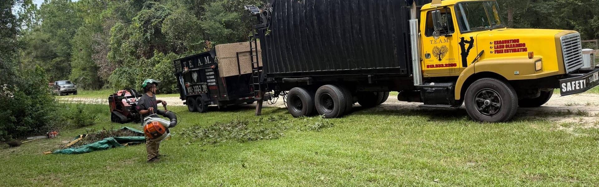 T.E.A.M. grapple truck, dump trailer, tracked loader, and crew at a Tampa Bay job site